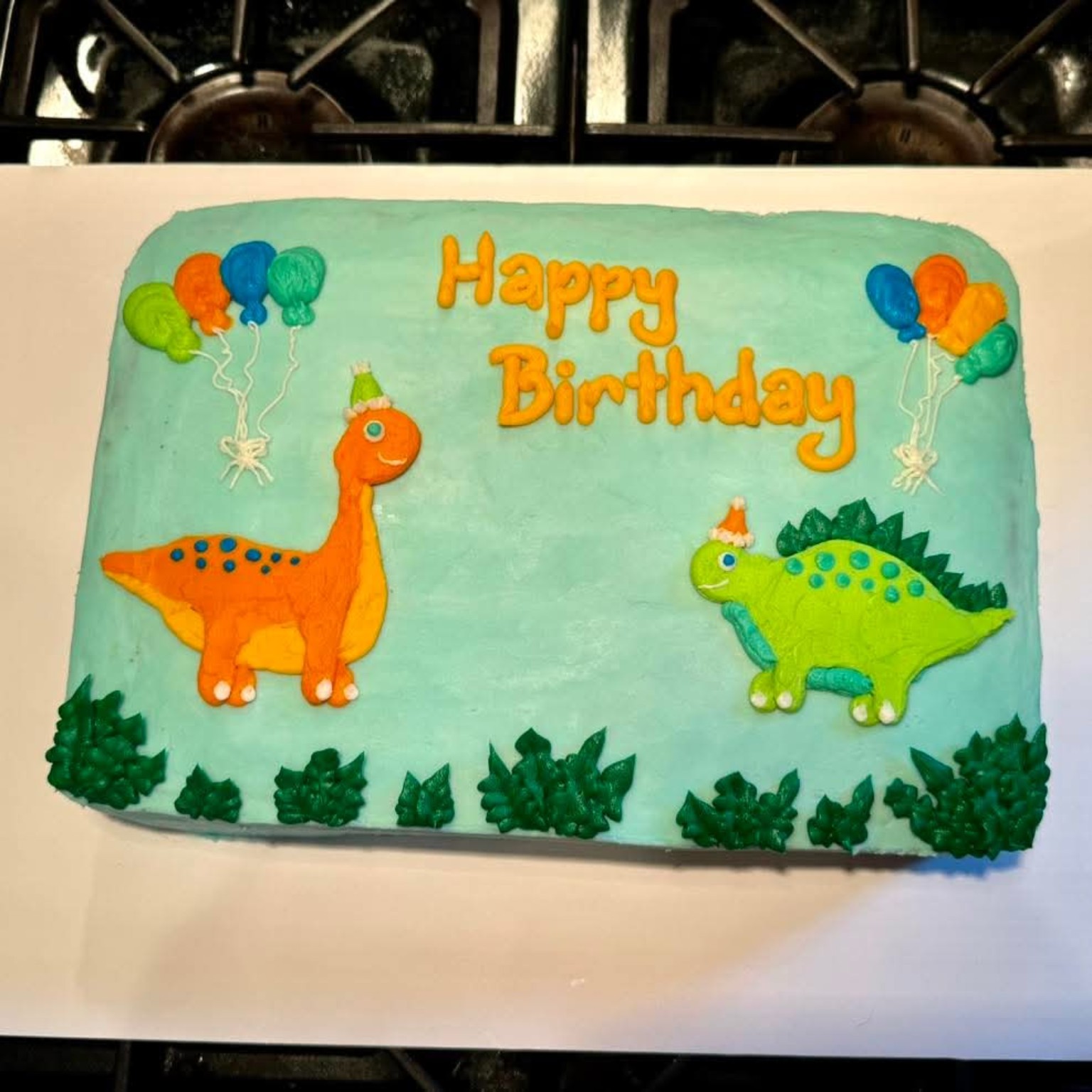 Children's birthday cake with blue frosting, cartoon dinosaurs, and balloon decorations