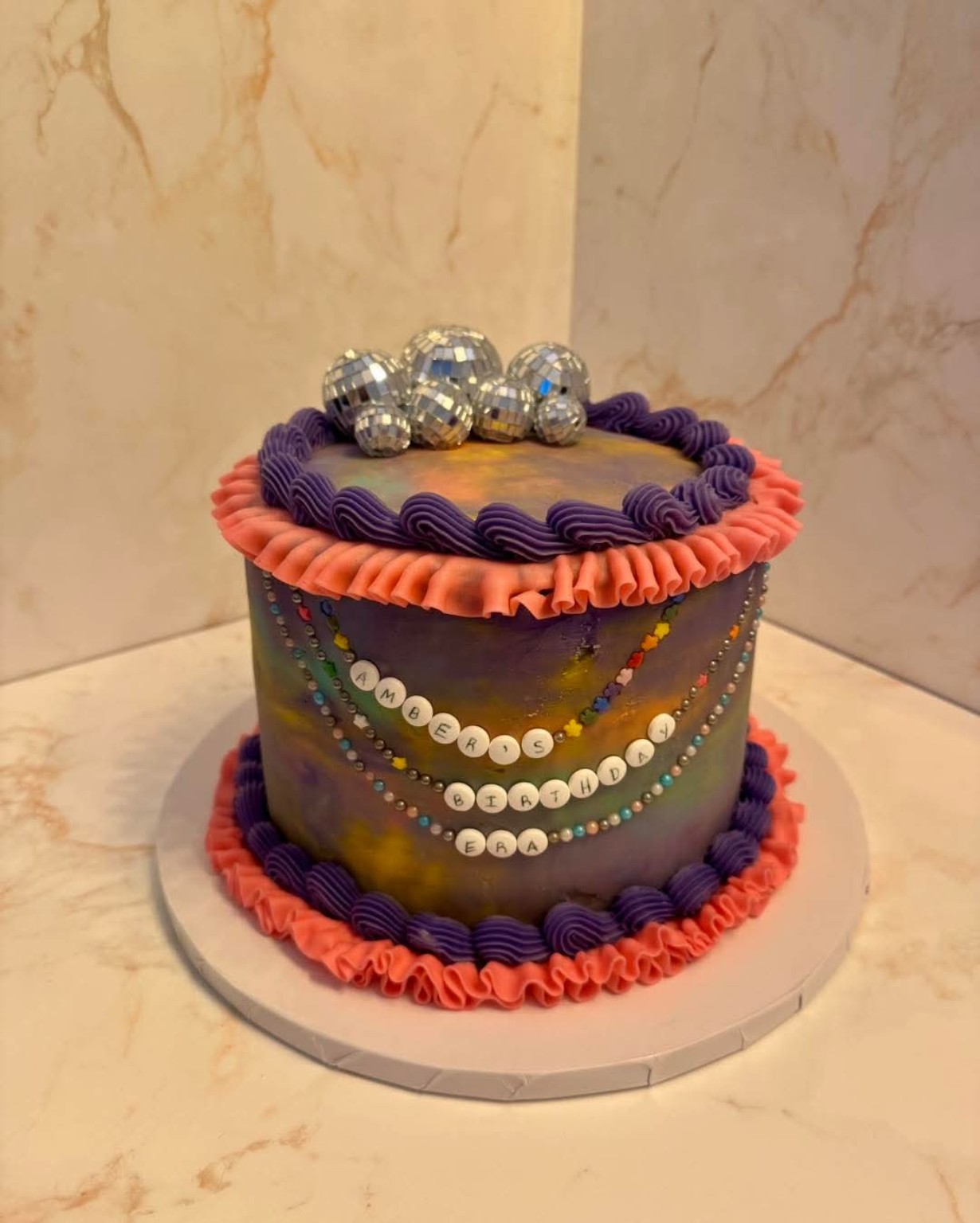 Custom birthday cake with iridescent swirl frosting, disco ball toppers, and friendship bracelet decorations