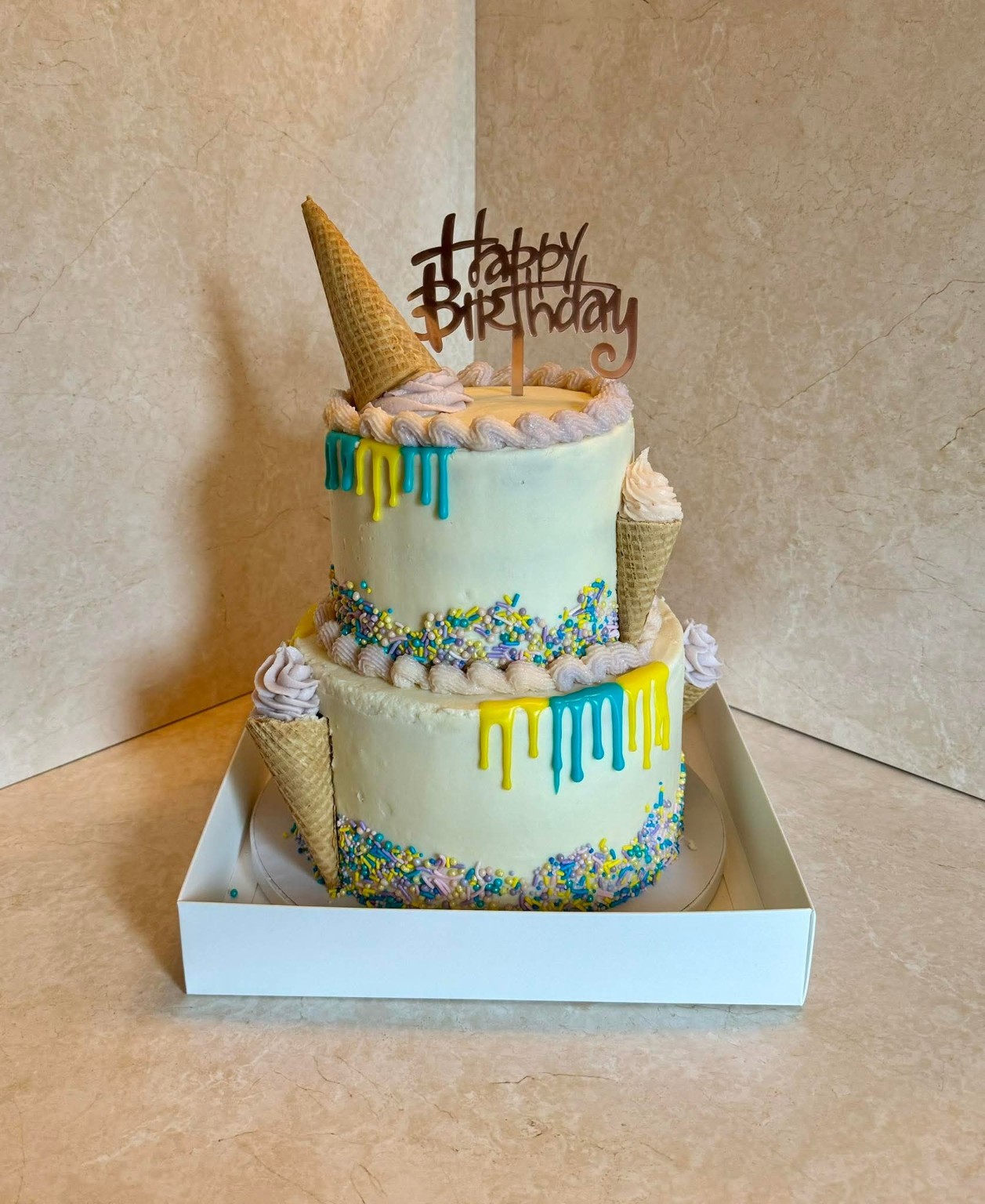 2-tier ice cream birthday cake with waffle cones, colorful drips, sprinkles, and a Happy Birthday topper