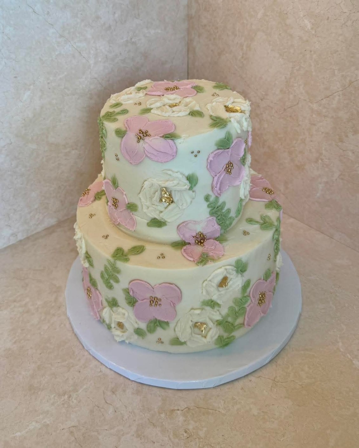 2-tier hand-painted floral cake with pink, lavender, and white buttercream flowers and gold details