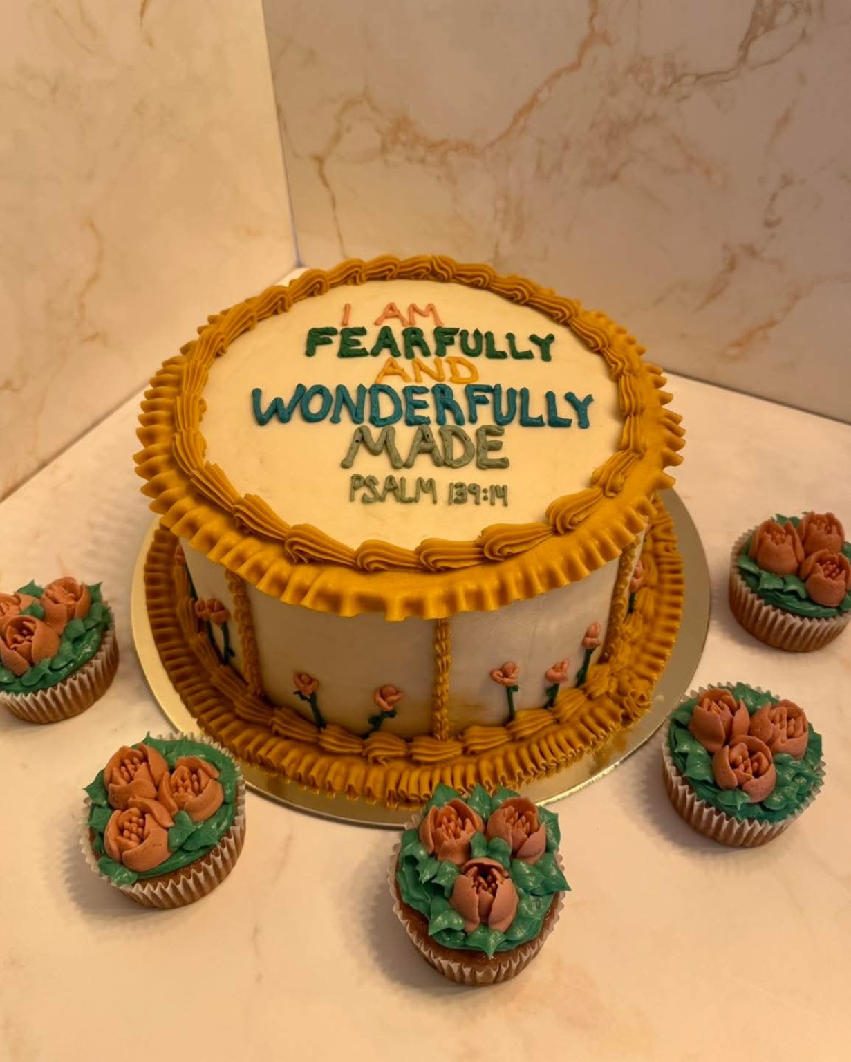 Round cake decorated with Psalm 139:14 scripture text, golden mustard ruffled border, and matching cupcakes