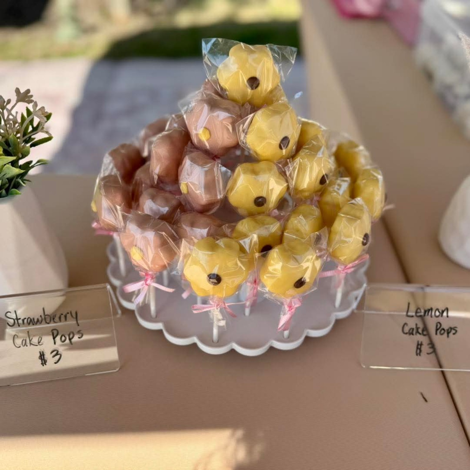 Strawberry and lemon cake pops displayed on a tiered stand at a market booth with price signs