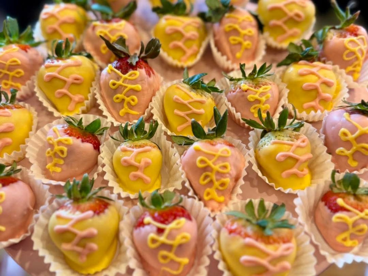 Chocolate-dipped strawberries in pink and yellow coating with decorative drizzle in cupcake liners