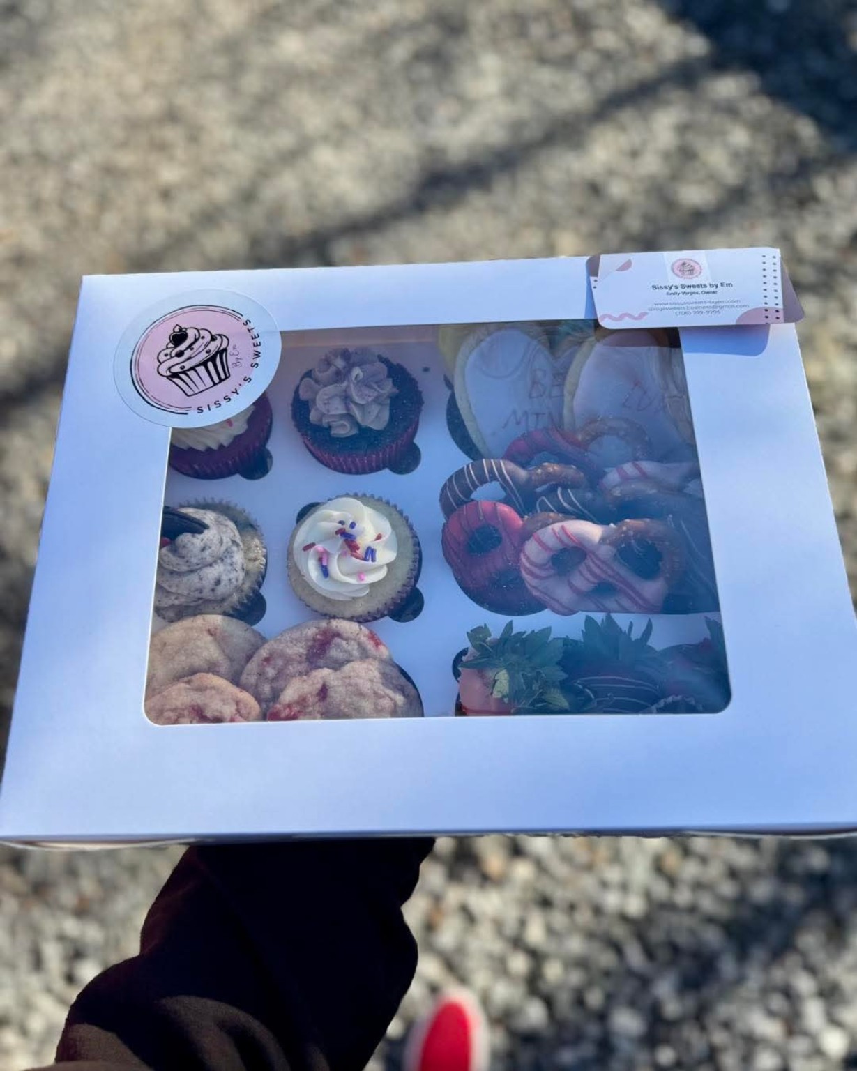 Sissy's Sweets branded treat box with cupcakes, cookies, and chocolate strawberries through a window display